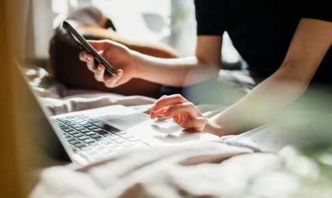 Person typing on laptop while looking at phone